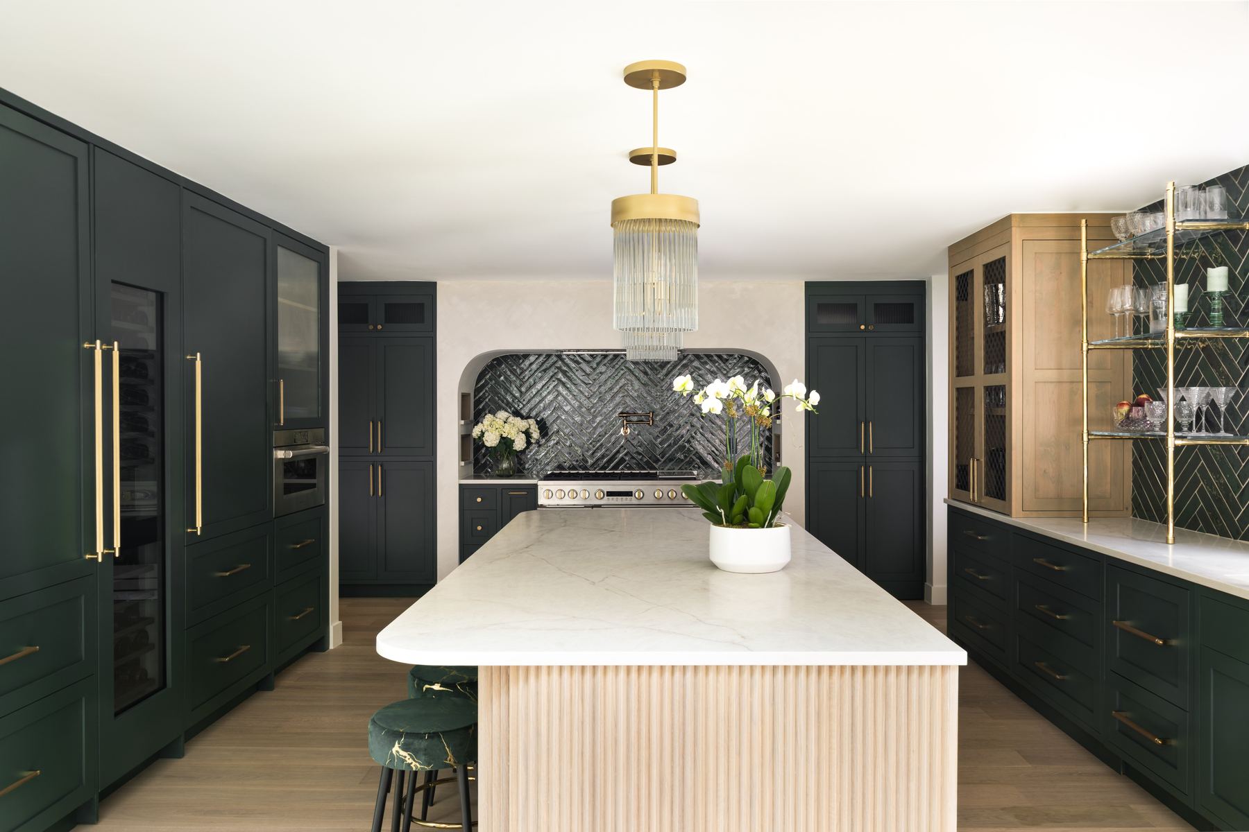 Hunter green kitchen cabinetry with brass fixtures and marble island